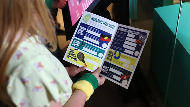 A child reads an Indigenous Trail booklet in front of museum display