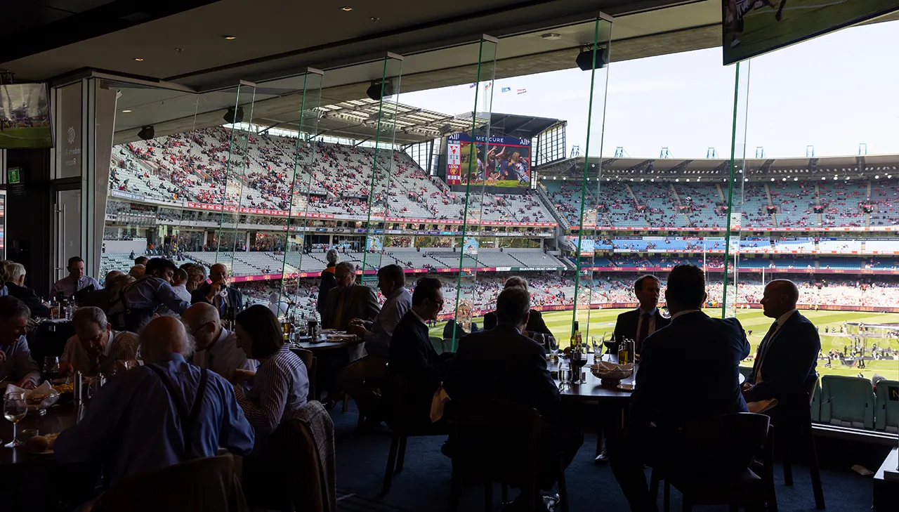 Patrons dining next to large windows with a view onto the MCG turf and seating
