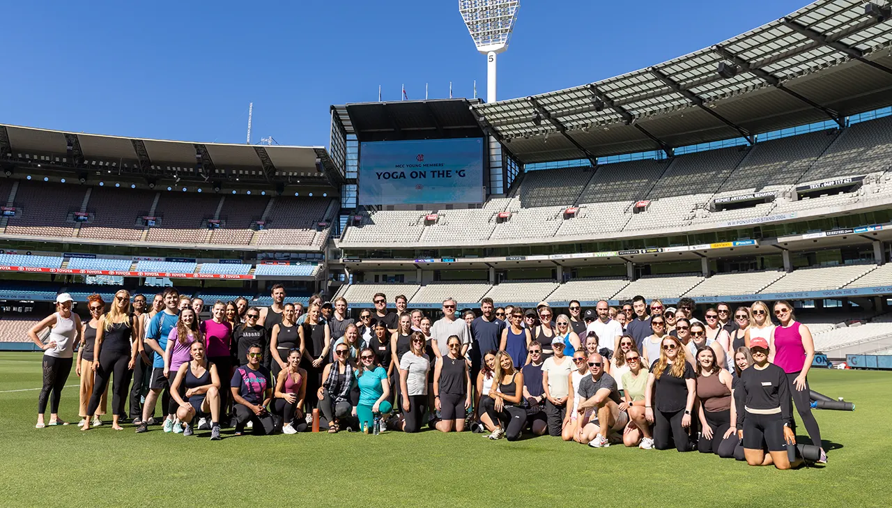 Group photo on the MCG turf of people in activewear. Sign says Yoga on the 'G.