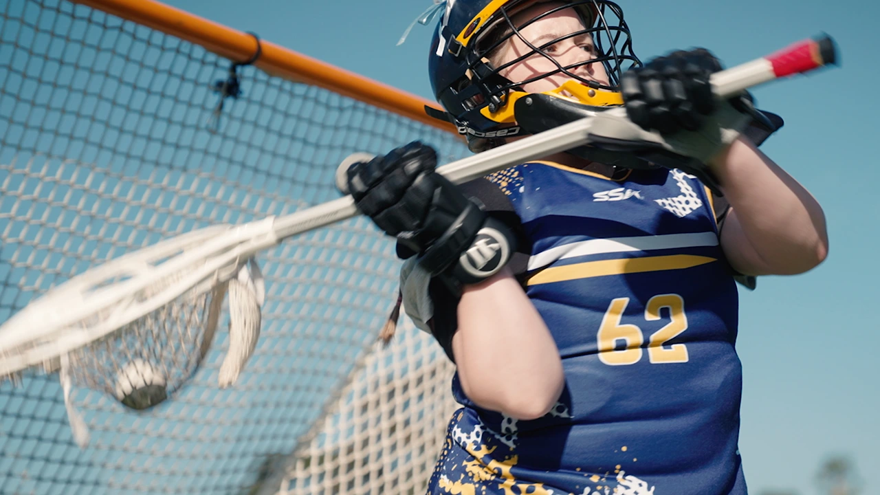 Lacrosse player in front of the goals in number 62 in blue and yellow