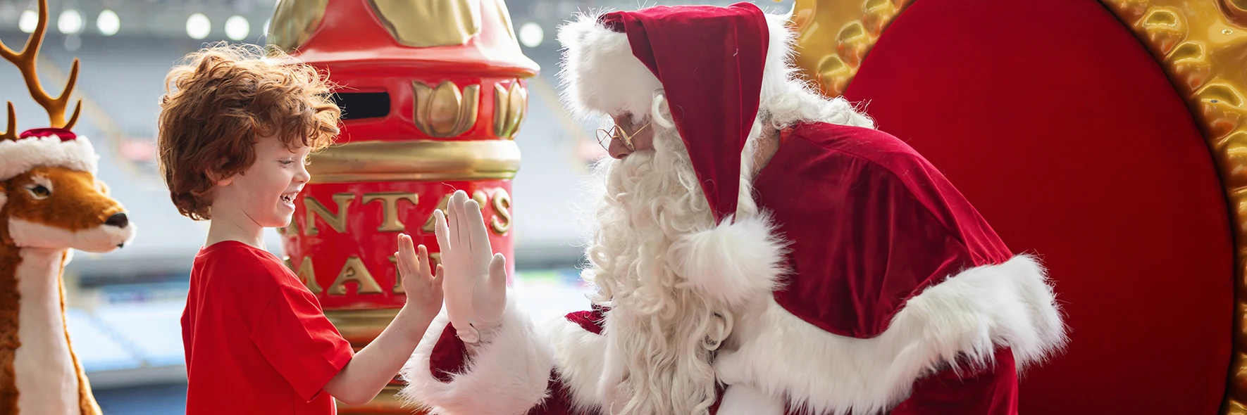 A young boy high-fiving Santa beside a red Santa's Mail postbox